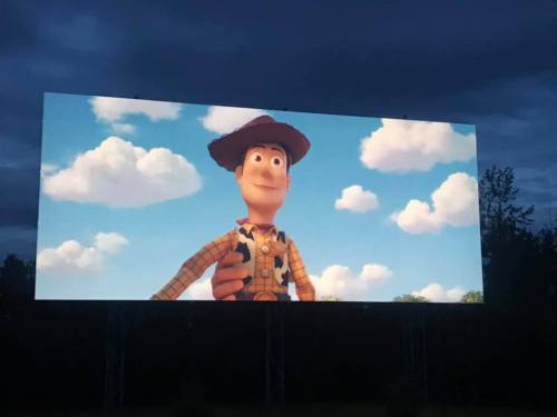 A large outdoor screen displays a character from an animated film, smiling against a blue sky with clouds.
