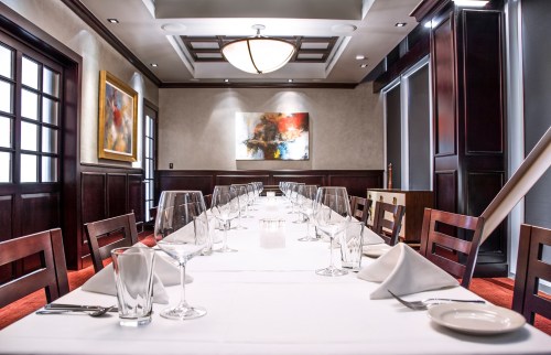 Elegant dining room with a long table set for a meal, featuring wine glasses and a modern art piece on the wall.