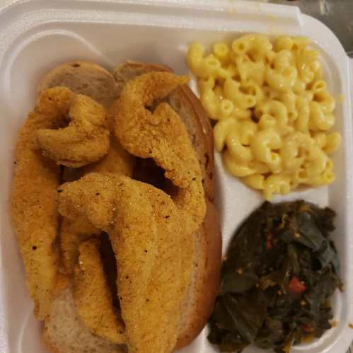 A styrofoam container with two pieces of fried fish on bread, macaroni and cheese, and collard greens.