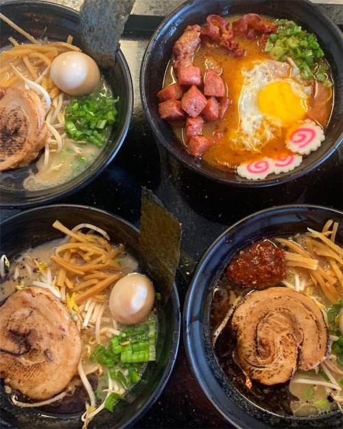 Four bowls of ramen with various toppings, including eggs, pork, green onions, and narutomaki, arranged on a table.