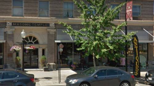 Facade of a historic building labeled "Masonic Temple," with a shop sign for "Antiques" and parked cars in front.