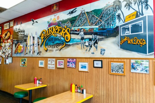 Colorful mural of Santa Cruz with hot dog stand, beach scenes, and vintage photos on a wooden wall in a casual eatery.