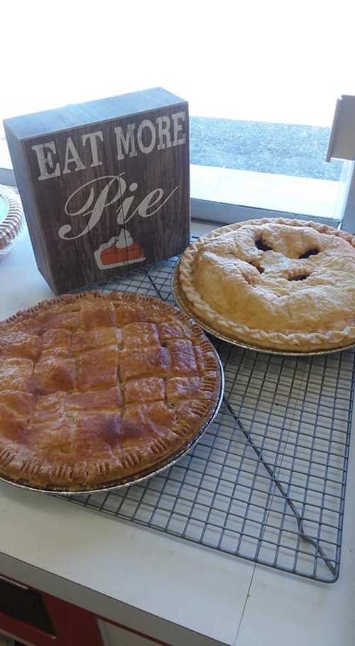 Two freshly baked pies on a cooling rack, with a sign that says "Eat More Pie" in the background.