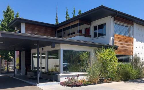 Modern two-story building with a mix of wood and white exterior, large windows, and landscaped greenery.