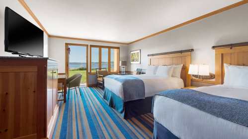 A cozy hotel room with two beds, a TV, and a view of the outdoors through sliding glass doors.