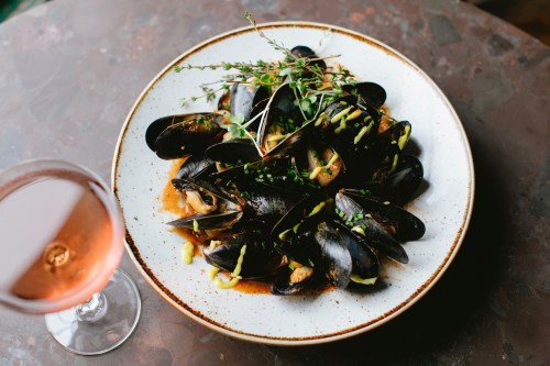 A plate of mussels garnished with herbs, accompanied by a glass of rosé wine.