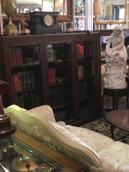 A vintage display cabinet filled with books, a decorative statue, and a floral-patterned sofa in a cozy interior.