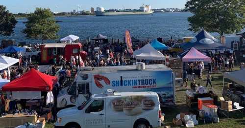 A bustling outdoor seafood festival by the water, featuring food trucks, tents, and a large crowd enjoying the event.