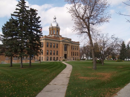 Historic building with a dome, surrounded by trees and a grassy path under a partly cloudy sky.