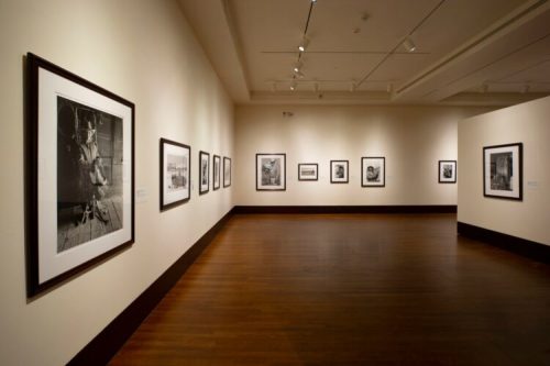 A gallery interior featuring framed black-and-white photographs on the walls and polished wooden flooring.