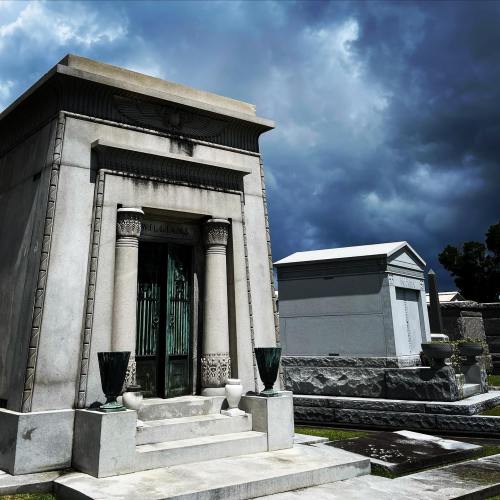 A grand mausoleum with ornate columns and a green door, set against a dramatic, cloudy sky.