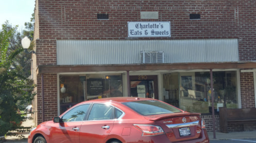 A red car parked in front of a brick building with a sign that reads "Charlotte's Eats & Sweets."