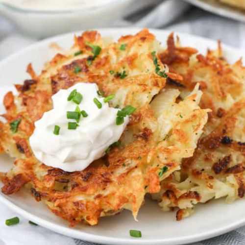 Crispy golden hash browns topped with sour cream and chives on a white plate.