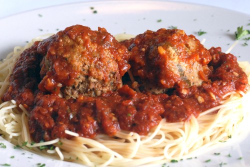 A plate of spaghetti topped with two large meatballs and marinara sauce, garnished with parsley.