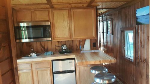 Cozy wooden kitchen with a microwave, fridge, and bar stools, featuring warm wood paneling and natural light.