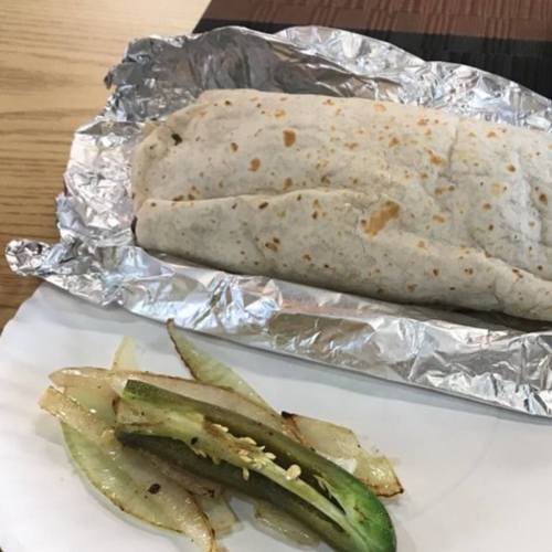 A wrapped burrito in foil next to a plate of sliced grilled vegetables.