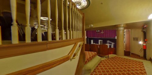 Interior view of a theater staircase leading to a seating area, featuring ornate railings and patterned carpet.