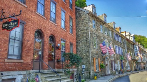 Historic buildings with American flags, featuring a brick inn and stone houses along a charming street.