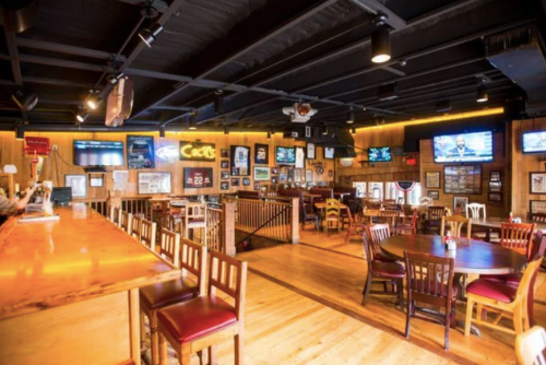 Interior of a cozy restaurant with wooden decor, tables, and multiple TVs displaying sports.