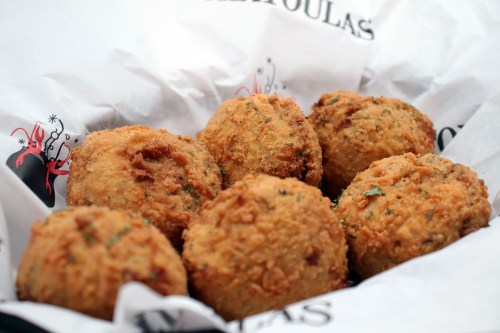 A basket of golden-brown, crispy fried balls, garnished with herbs, resting on patterned paper.