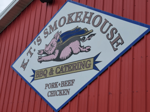 Sign for K.T.'s Smokehouse BBQ & Catering featuring a pig graphic, with text highlighting pork, beef, and chicken options.