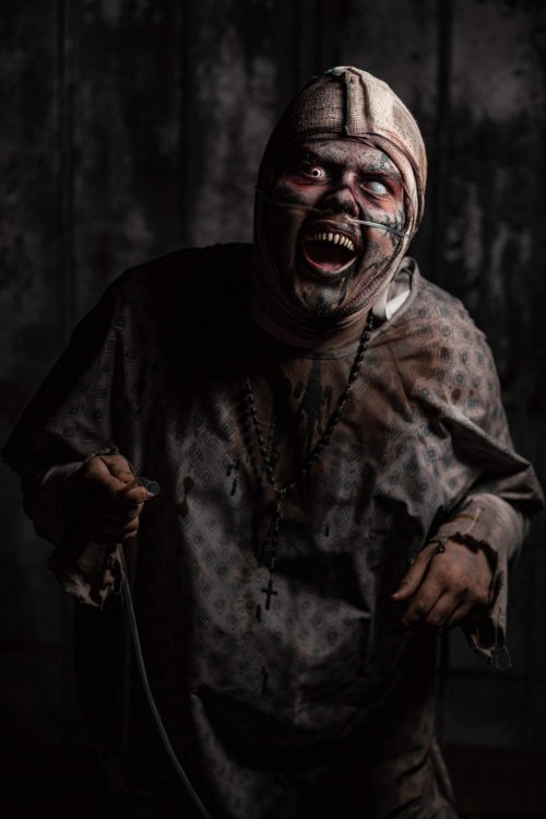 A sinister figure in tattered clothing and a bandaged face, grinning menacingly in a dark, eerie setting.