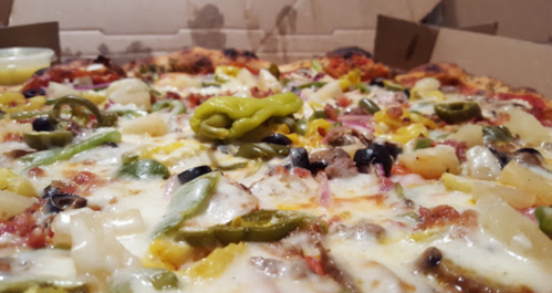 A close-up of a pizza topped with various vegetables, cheese, and meats, inside a pizza box.