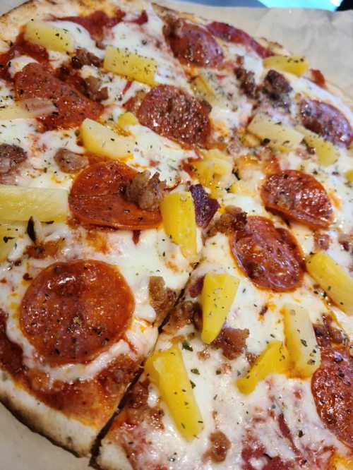 A close-up of a pizza topped with pepperoni, pineapple, and cheese, with a crispy crust.