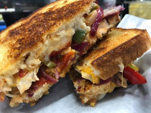 Close-up of a grilled sandwich filled with melted cheese, colorful peppers, and onions, with crispy golden-brown bread.