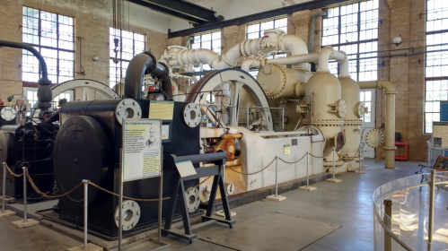 Historic industrial machinery displayed in a spacious, well-lit museum setting with large windows.