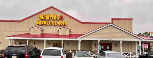 Exterior of Memphis Barbecue Co. restaurant with a red roof and sign, surrounded by parked cars.