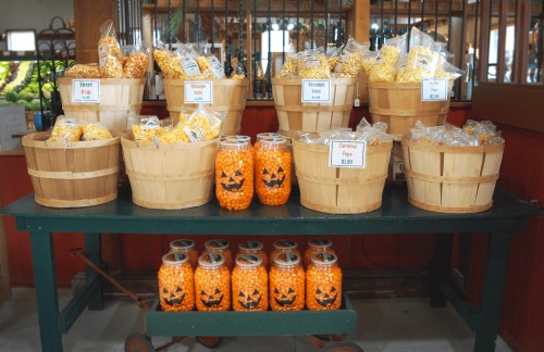 A display of popcorn in wooden baskets and jars, featuring Halloween-themed decorations.