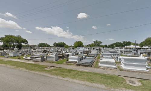 A wide view of a cemetery with numerous gravestones and monuments under a clear blue sky.