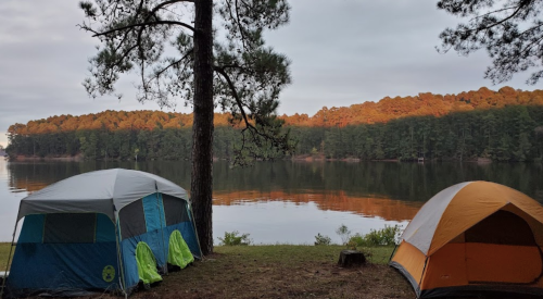 Two tents by a calm lake, surrounded by trees and reflecting autumn colors in the water.