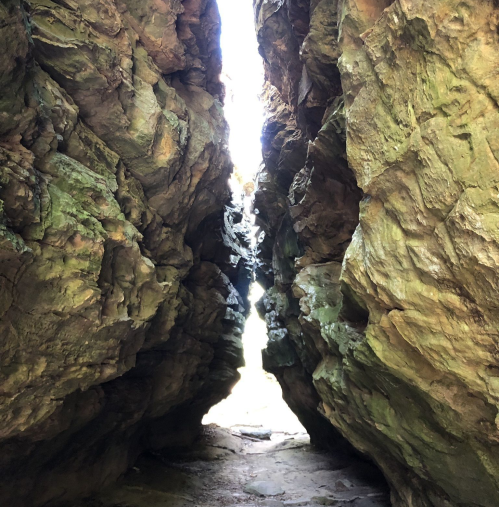 A narrow rock crevice with towering stone walls, leading to bright light in the distance.