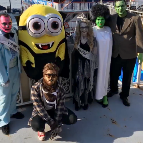 A group of six people in costumes, including a Minion, posing together at an outdoor event.