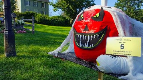A large, spooky pumpkin decoration with a menacing face, draped in white cobwebs, stands in a grassy area.