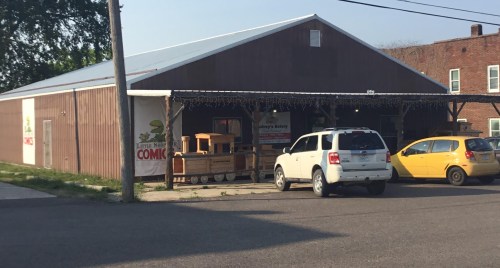 A wooden building with a metal roof, featuring a sign for a comic store, parked cars, and a clear blue sky.