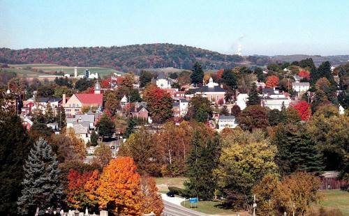 A scenic view of a small town surrounded by colorful autumn trees and rolling hills in the background.