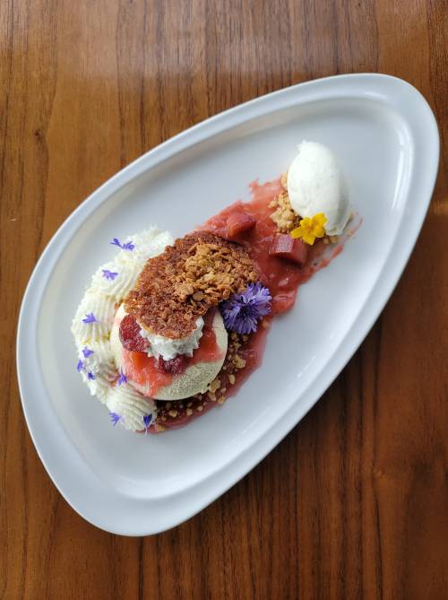 A beautifully plated dessert featuring layers of fruit, cream, and crumble, garnished with edible flowers and ice cream.