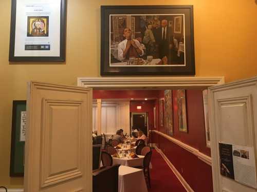 A view of a restaurant interior with framed artwork on the walls and diners at tables in the background.