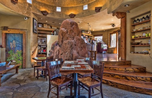 Cozy restaurant interior featuring wooden tables, a large rock centerpiece, and warm, earthy decor.
