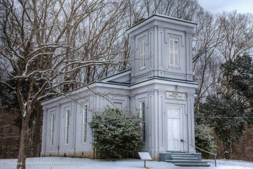 A gray building with a unique architectural design, surrounded by snow-covered trees in a winter landscape.