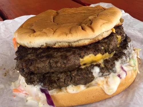 A large burger with two thick beef patties, melted cheese, and creamy coleslaw, served in a toasted bun.