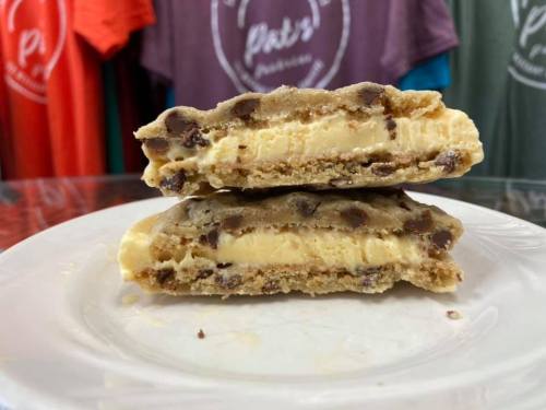 Two layers of cookie dough with chocolate chips and creamy filling, stacked on a white plate. Colorful shirts in the background.