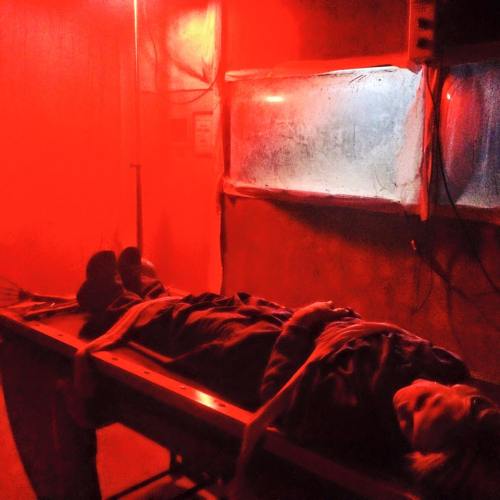 A dimly lit room with red lighting, featuring a person lying on a medical stretcher.