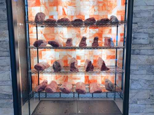 A display case with various cuts of meat arranged on shelves, illuminated by a warm, glowing background.