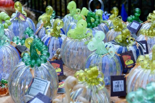 A collection of colorful glass pumpkins in various shapes and sizes, displayed on a wooden surface.