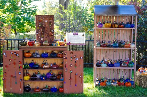 Colorful decorative pumpkins displayed on wooden shelves in a garden setting, surrounded by greenery.