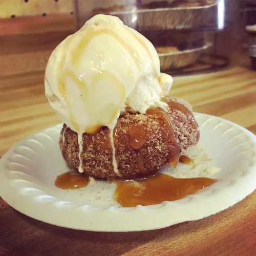 A warm donut topped with a scoop of ice cream and drizzled with caramel sauce on a paper plate.